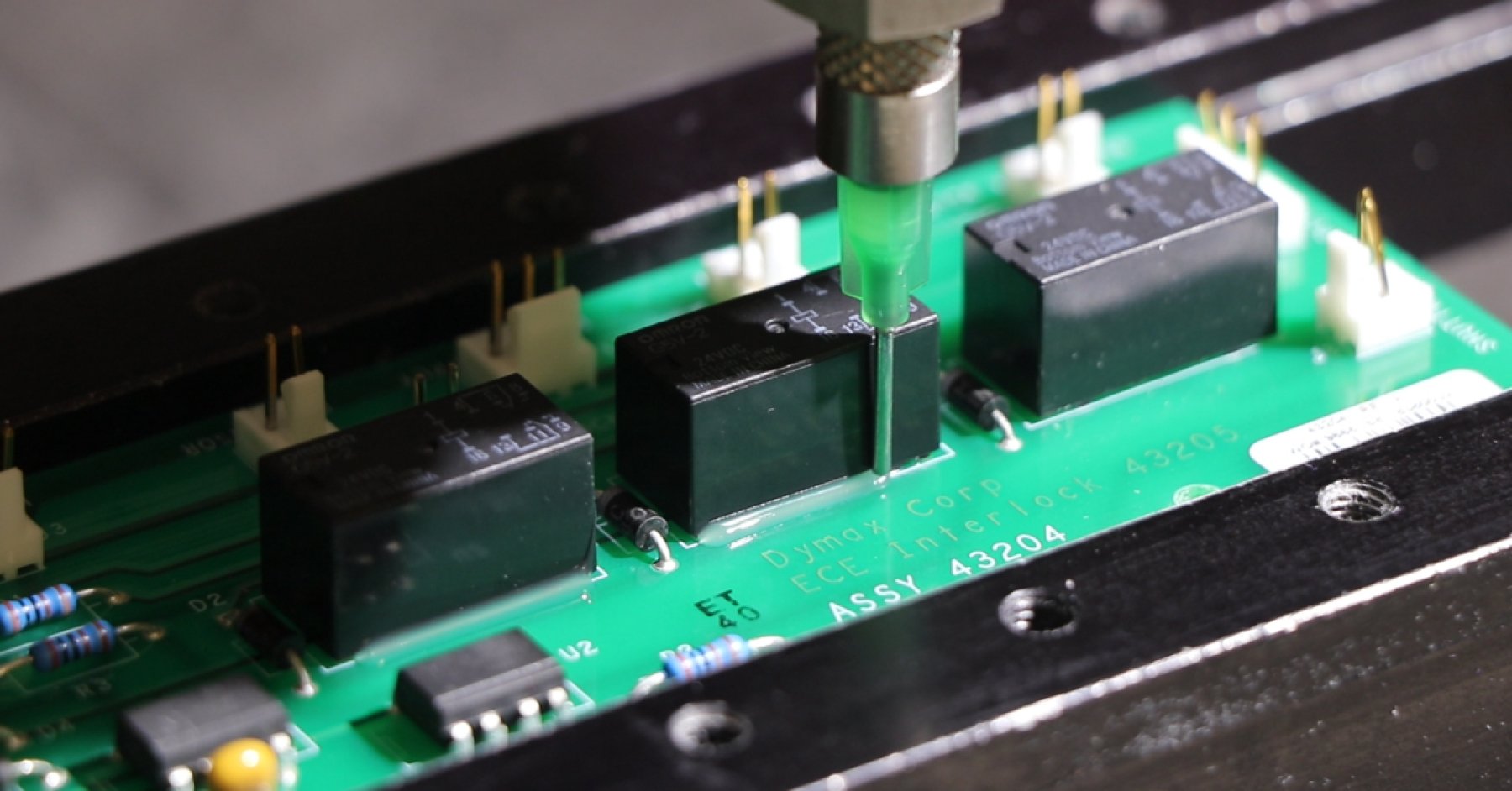Dymax adhesive being dispensed around a component to secure it to a printed circuit board.