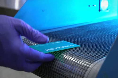 An operator places a printed circuit board onto a UV light-curing conveyor.